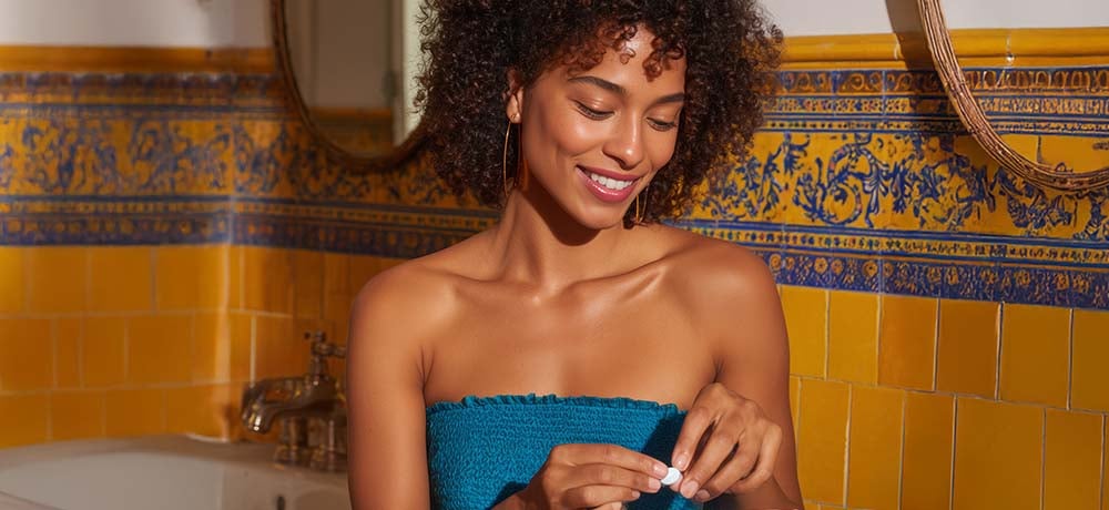 Smiling woman in a bathroom holding a white capsule