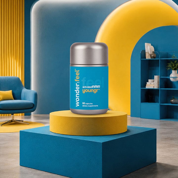 Wonderfeel Youngr™ NMN supplement bottle displayed on a yellow and teal pedestal in a stylish blue and yellow room with an armchair and bookshelf in the background.