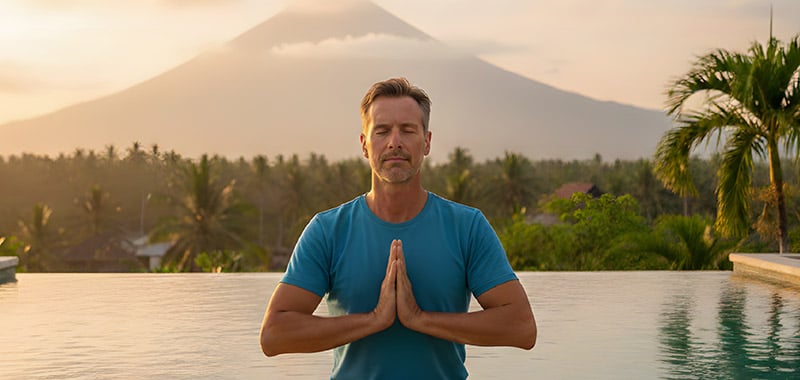 Man meditating outdoors near a pool with a mountain landscape in the background, representing healthy aging through stress management, mindfulness, and lifestyle habits that support long-term vitality.